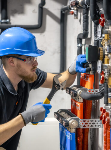 The technician checking the heating system in the boiler room. Adjusting heating valves in a residential building. A plumbing and heating technician works.